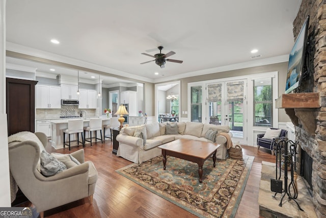 living area with a stone fireplace, a ceiling fan, ornamental molding, recessed lighting, and wood finished floors