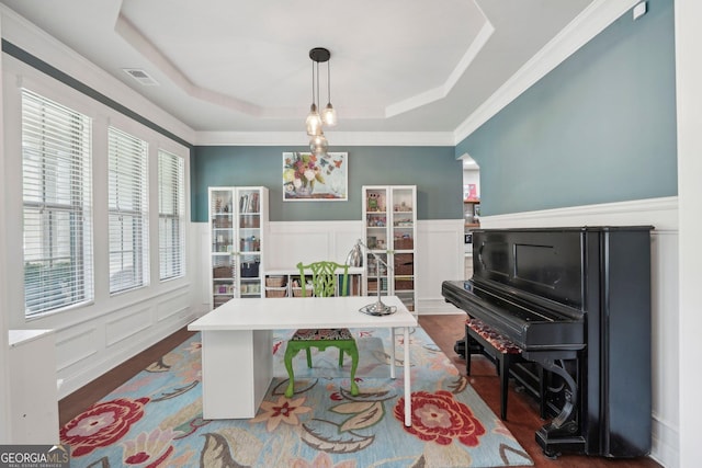 office area featuring a tray ceiling, a decorative wall, dark wood-type flooring, wainscoting, and ornamental molding
