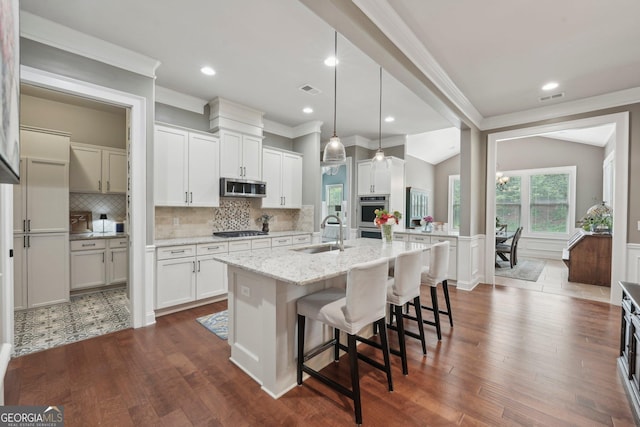 kitchen featuring a sink, stainless steel appliances, ornamental molding, an island with sink, and backsplash
