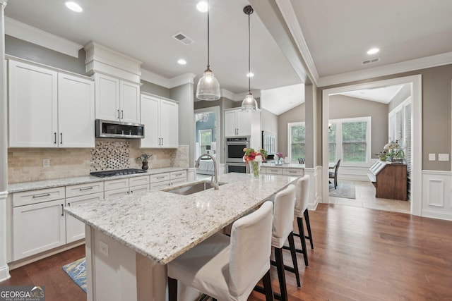 kitchen with a sink, stainless steel appliances, a center island with sink, white cabinetry, and a kitchen bar
