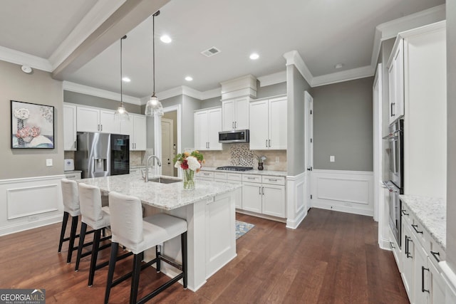kitchen with appliances with stainless steel finishes, a sink, crown molding, white cabinetry, and a center island with sink