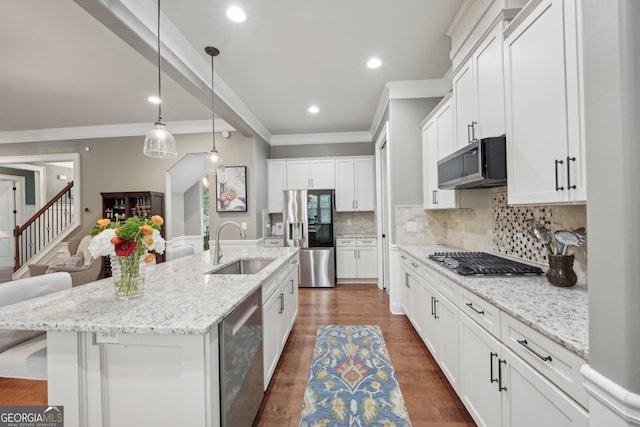 kitchen featuring stainless steel appliances, a sink, crown molding, decorative backsplash, and a center island with sink