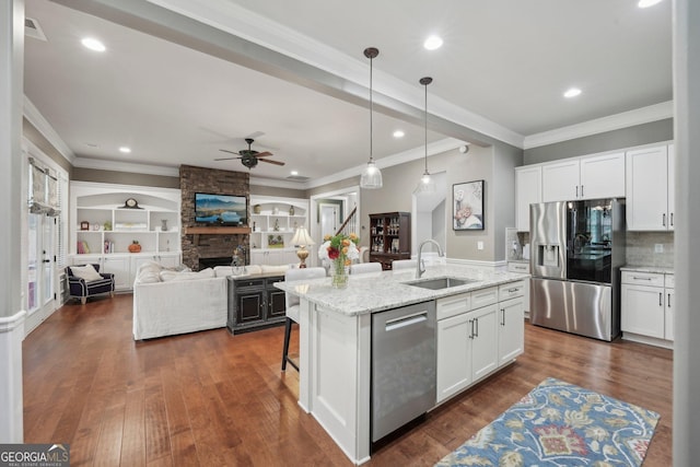 kitchen with stainless steel appliances, a sink, ceiling fan, a fireplace, and white cabinetry