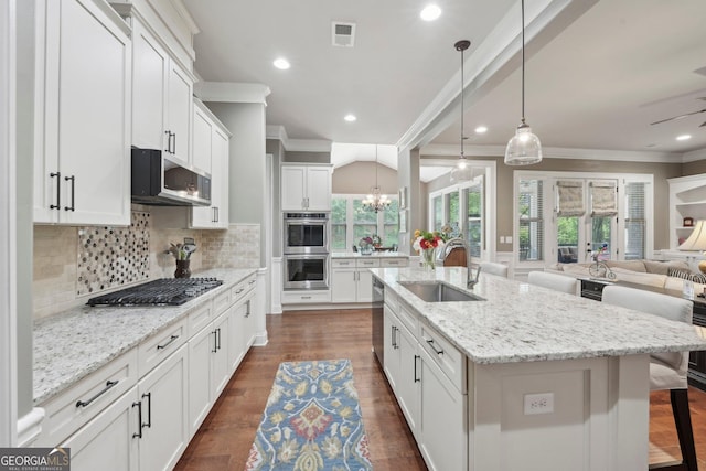 kitchen with appliances with stainless steel finishes, a sink, ornamental molding, open floor plan, and a kitchen bar