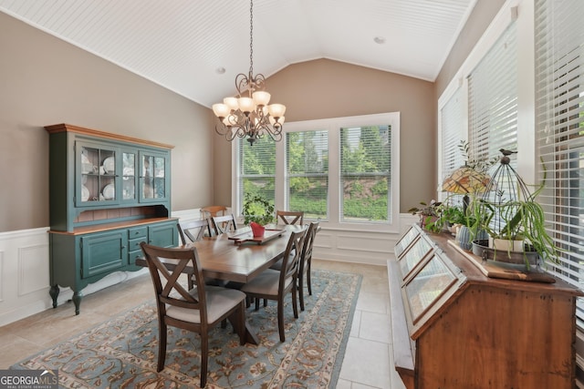 dining space with a decorative wall, wainscoting, a chandelier, vaulted ceiling, and light tile patterned flooring