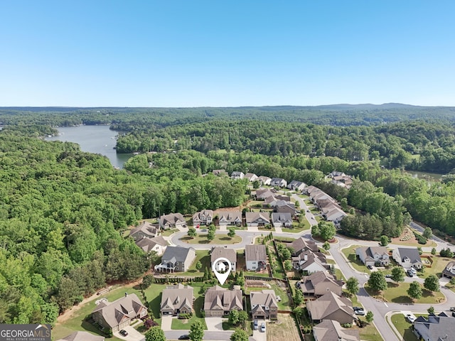 aerial view of property's location featuring a forest, a nearby body of water, and nearby suburban area