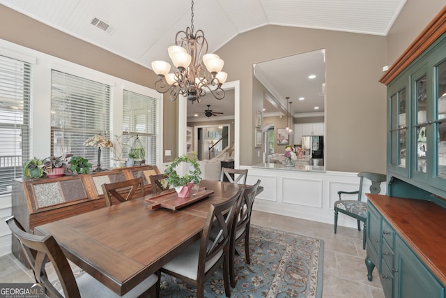 dining area featuring vaulted ceiling, a chandelier, ceiling fan, a wainscoted wall, and crown molding