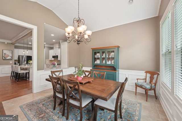 dining room with a decorative wall, crown molding, a chandelier, wainscoting, and lofted ceiling