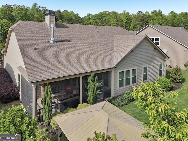 back of house featuring roof with shingles, a chimney, and a sunroom