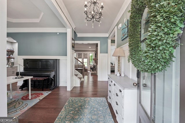 foyer entrance featuring stairs, dark wood finished floors, a chandelier, crown molding, and a decorative wall