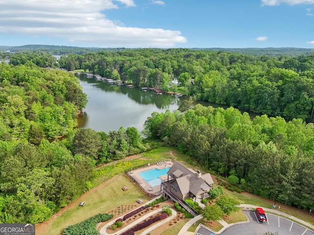 aerial view of a heavily wooded area, a nearby body of water, and a pool