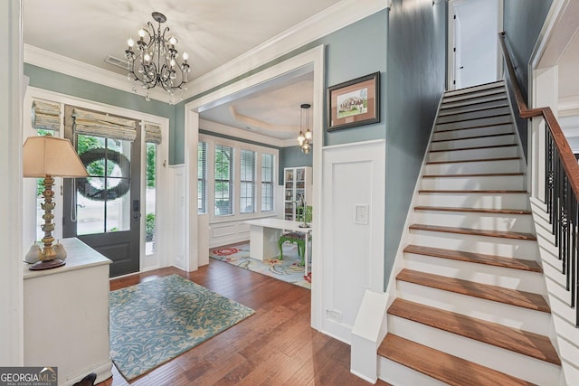 foyer entrance with a chandelier, ornamental molding, stairway, and hardwood / wood-style floors