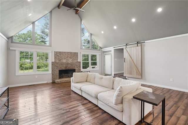 living area with high vaulted ceiling, beamed ceiling, wood finished floors, a ceiling fan, and a barn door
