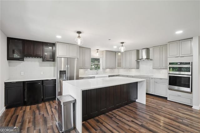 kitchen with wall chimney range hood, stainless steel appliances, light countertops, decorative backsplash, and dark wood finished floors
