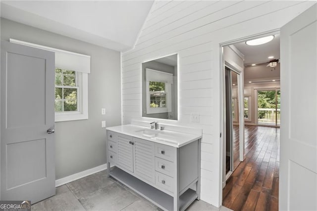 bathroom with healthy amount of natural light, lofted ceiling, vanity, wooden walls, and baseboards