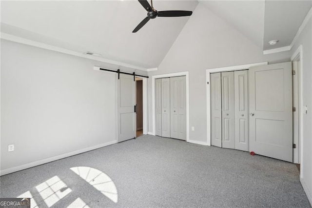 unfurnished bedroom with high vaulted ceiling, two closets, a barn door, carpet, and baseboards