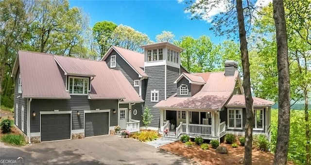view of front of property featuring driveway, a porch, a chimney, a garage, and metal roof