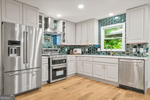 kitchen with stainless steel appliances, wall chimney range hood, a sink, light countertops, and tasteful backsplash
