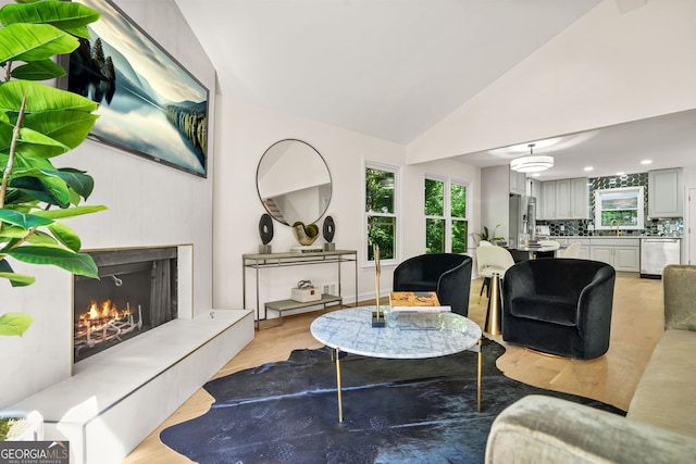 living area with a warm lit fireplace, vaulted ceiling, and light wood-style floors