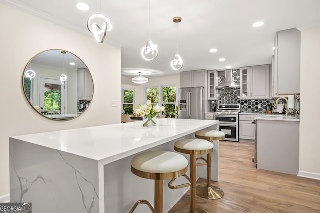 kitchen featuring appliances with stainless steel finishes, gray cabinets, wall chimney exhaust hood, a sink, and crown molding
