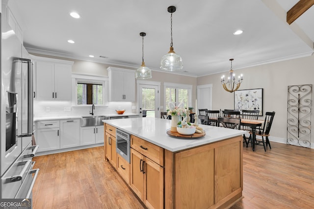 kitchen with appliances with stainless steel finishes, a sink, healthy amount of natural light, light countertops, and ornamental molding
