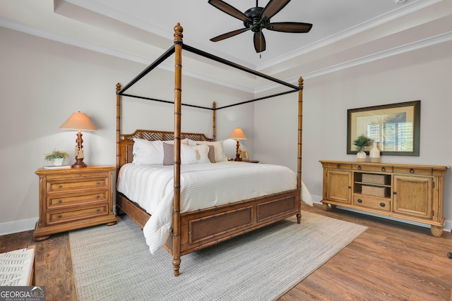 bedroom featuring a raised ceiling, wood finished floors, baseboards, and ornamental molding