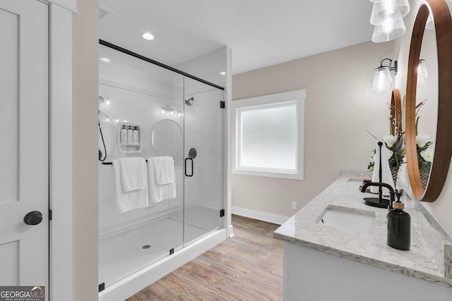 bathroom with a stall shower, baseboards, double vanity, wood finished floors, and recessed lighting