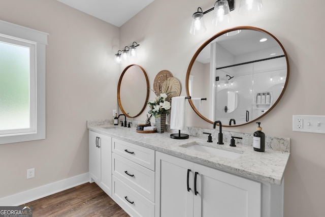 full bath featuring wood finished floors, baseboards, a shower, and double vanity