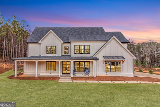 back of property featuring a shingled roof, covered porch, a lawn, and board and batten siding