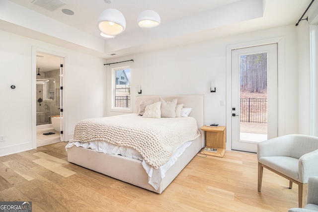 bedroom featuring light wood finished floors, access to outside, a tray ceiling, ensuite bathroom, and baseboards