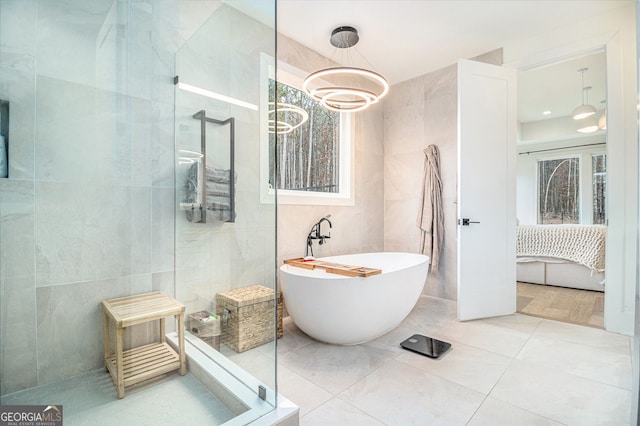 full bathroom featuring tile walls, walk in shower, a freestanding bath, a chandelier, and connected bathroom