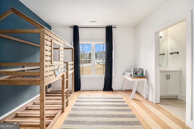 unfurnished bedroom featuring wood finished floors, baseboards, and connected bathroom