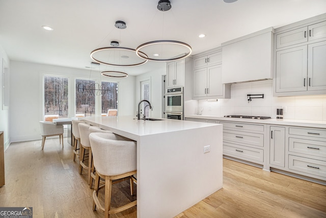 kitchen with a sink, light countertops, light wood-type flooring, an island with sink, and recessed lighting