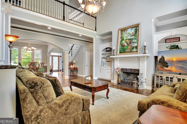 living area with ornate columns, a chandelier, arched walkways, a fireplace, and wood finished floors