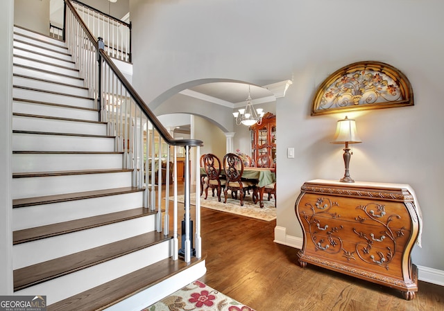entrance foyer with arched walkways, a chandelier, ornamental molding, baseboards, and stairway