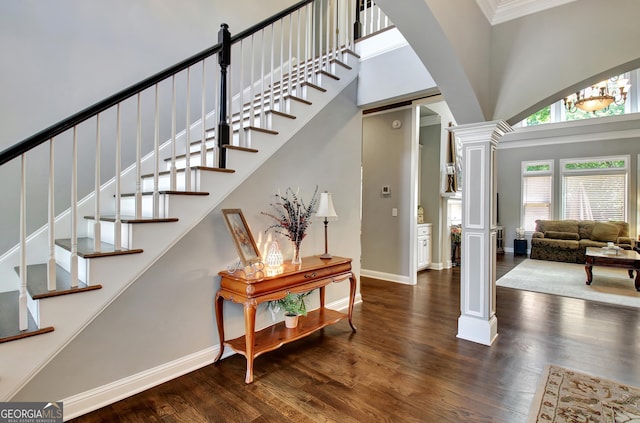 staircase featuring ornate columns, a towering ceiling, wood finished floors, baseboards, and ornamental molding