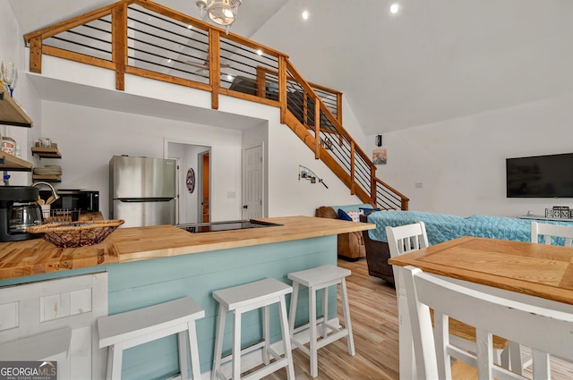 kitchen with freestanding refrigerator, high vaulted ceiling, black electric stovetop, butcher block countertops, and wood finished floors
