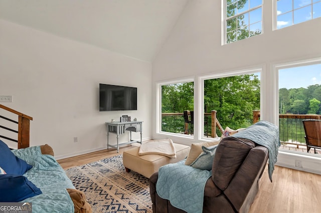 living room with high vaulted ceiling, plenty of natural light, light wood finished floors, and baseboards