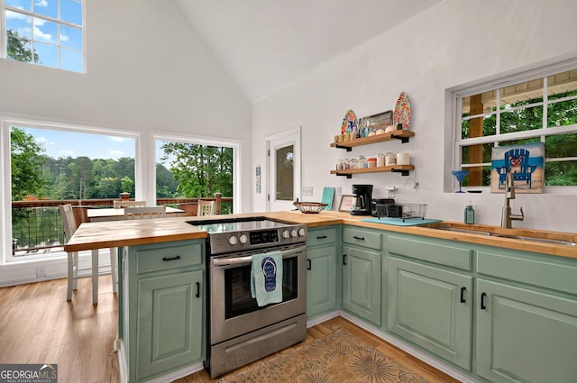 kitchen with wood counters, stainless steel electric stove, a sink, green cabinets, and high vaulted ceiling
