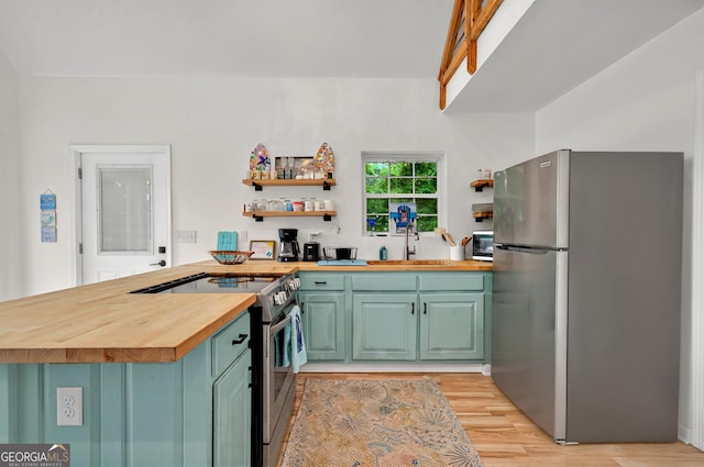 kitchen with appliances with stainless steel finishes, butcher block counters, a sink, light wood-style floors, and a peninsula