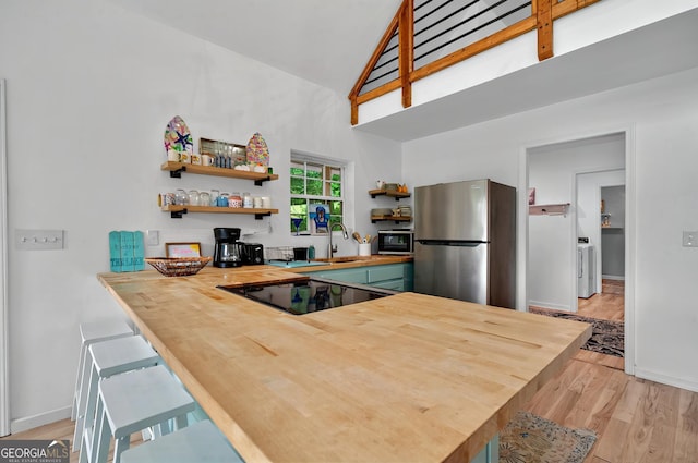 kitchen with freestanding refrigerator, butcher block countertops, open shelves, black electric cooktop, and a peninsula