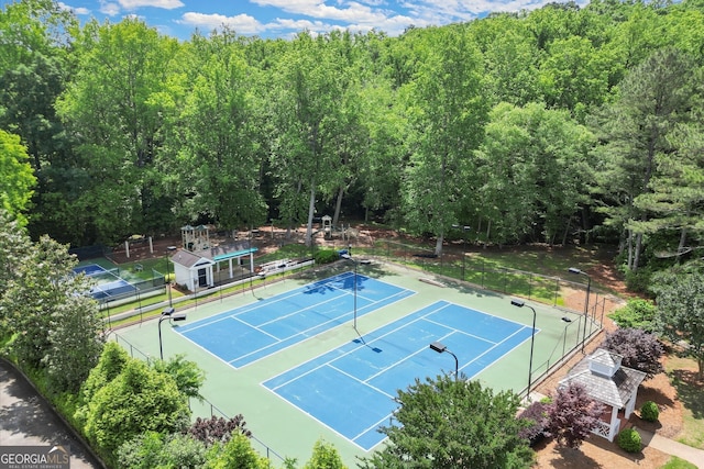 view of tennis court with fence and a wooded view