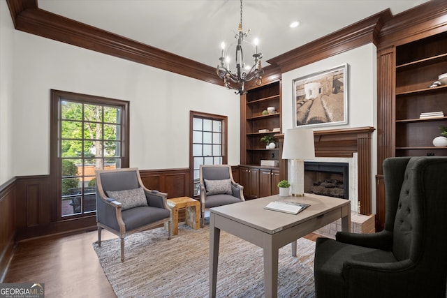 living area with ornamental molding, built in shelves, a chandelier, a wainscoted wall, and wood finished floors
