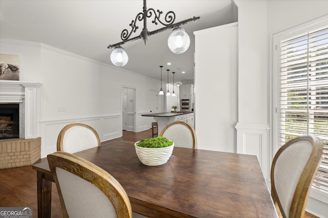 dining room featuring dark wood finished floors, crown molding, and a brick fireplace