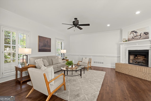 living area with ornamental molding, a ceiling fan, dark wood-style floors, wainscoting, and a fireplace with raised hearth