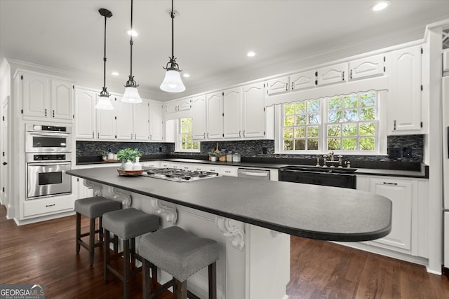 kitchen featuring dark countertops, backsplash, white cabinets, stainless steel appliances, and a sink