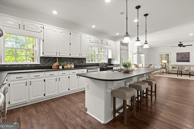 kitchen with dark countertops, open floor plan, decorative backsplash, a center island, and white cabinets