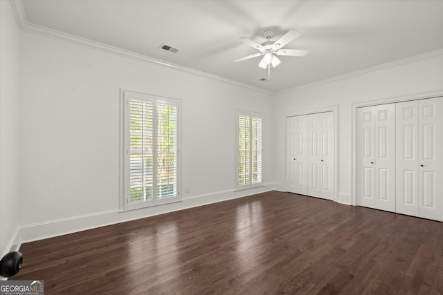 unfurnished bedroom featuring dark wood finished floors, ornamental molding, two closets, and baseboards