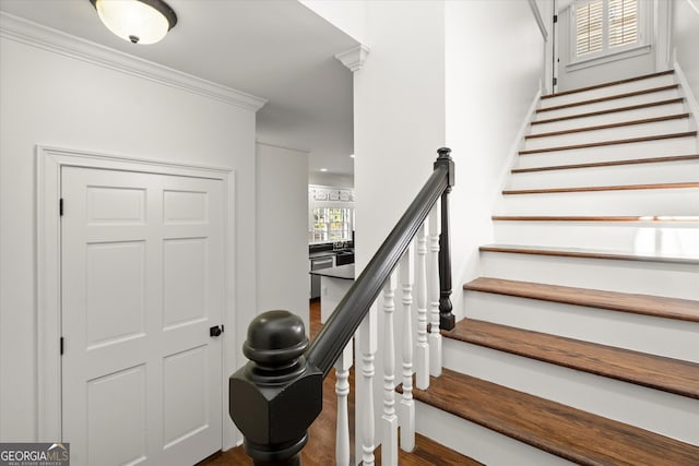 staircase with wood finished floors and ornamental molding