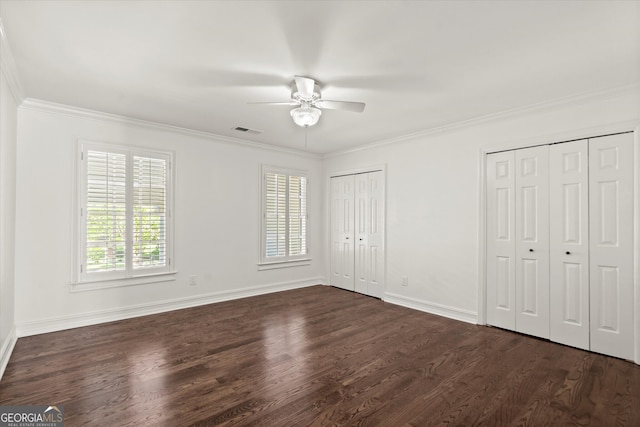 unfurnished bedroom with multiple closets, dark wood finished floors, multiple windows, crown molding, and baseboards